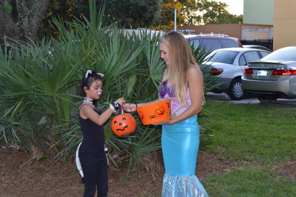 Young woman dressed as Ariel hands candy to girl dressed as cat